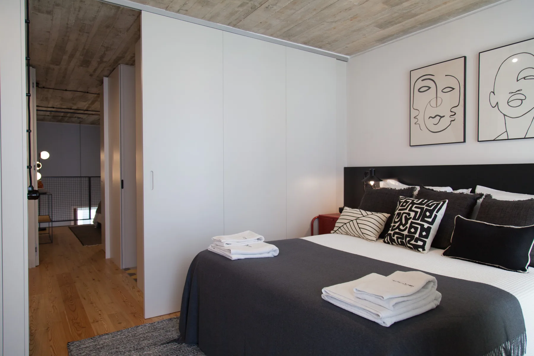 Dormitorio con una cama hecha, toallas dobladas y cuadros sobre el cabecero.