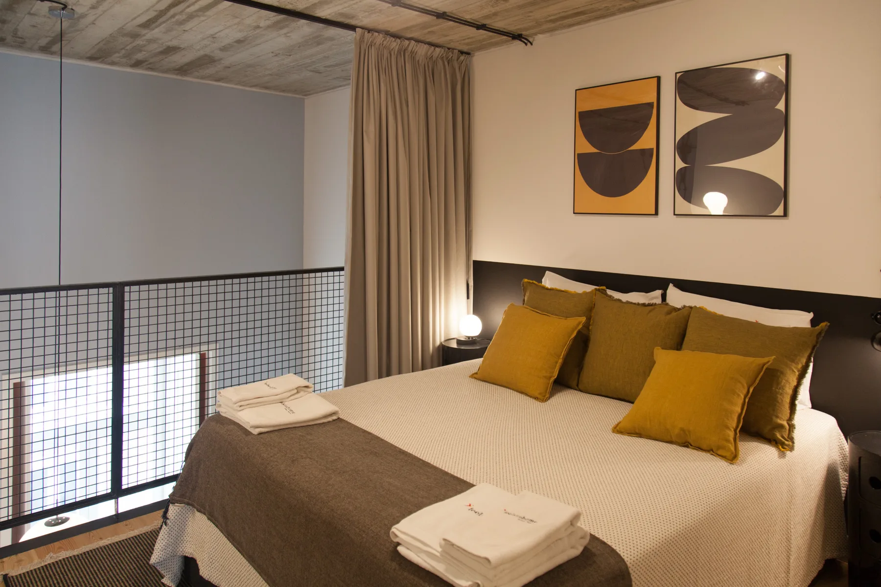 Un dormitorio con una cama doble y cojines color mostaza junto a una barandilla.