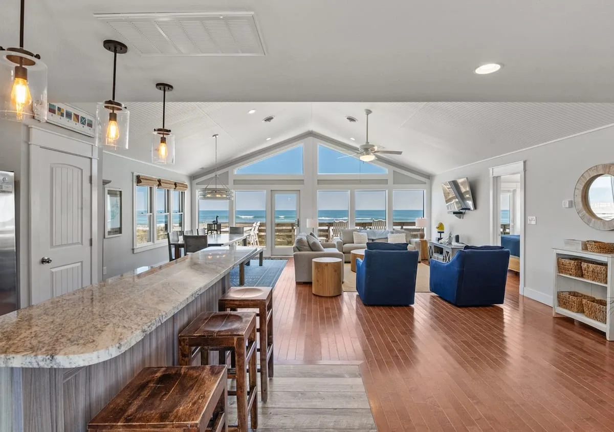 Una luminosa sala de estar y comedor de concepto abierto, con una larga barra de cocina y grandes ventanas.