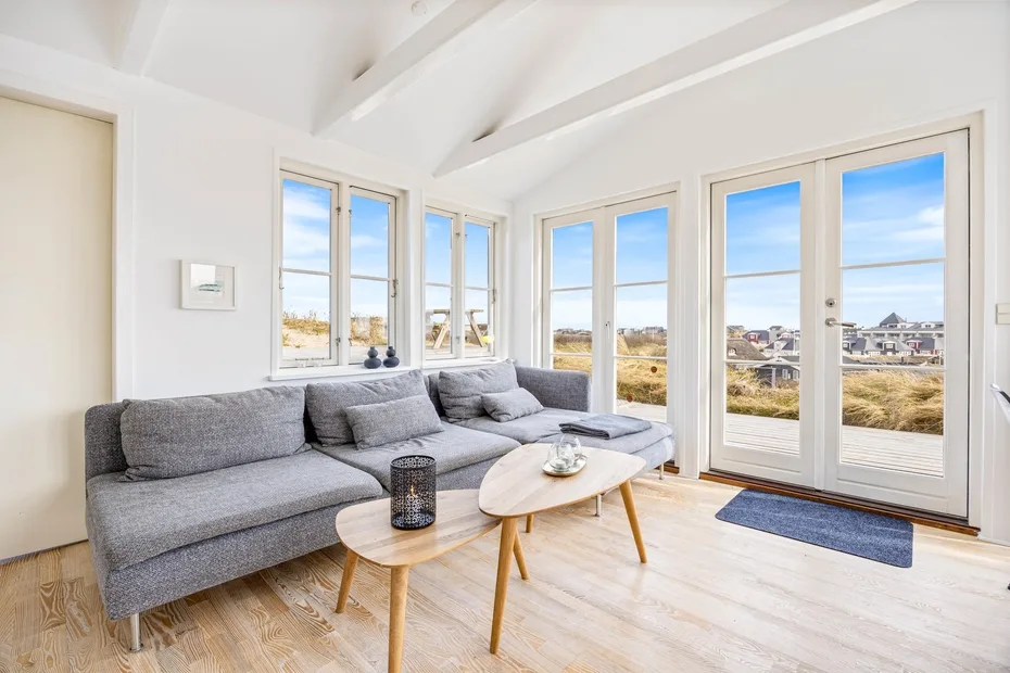 Una sala luminosa con asientos grises, mesas de centro y ventanas con vistas al paisaje.