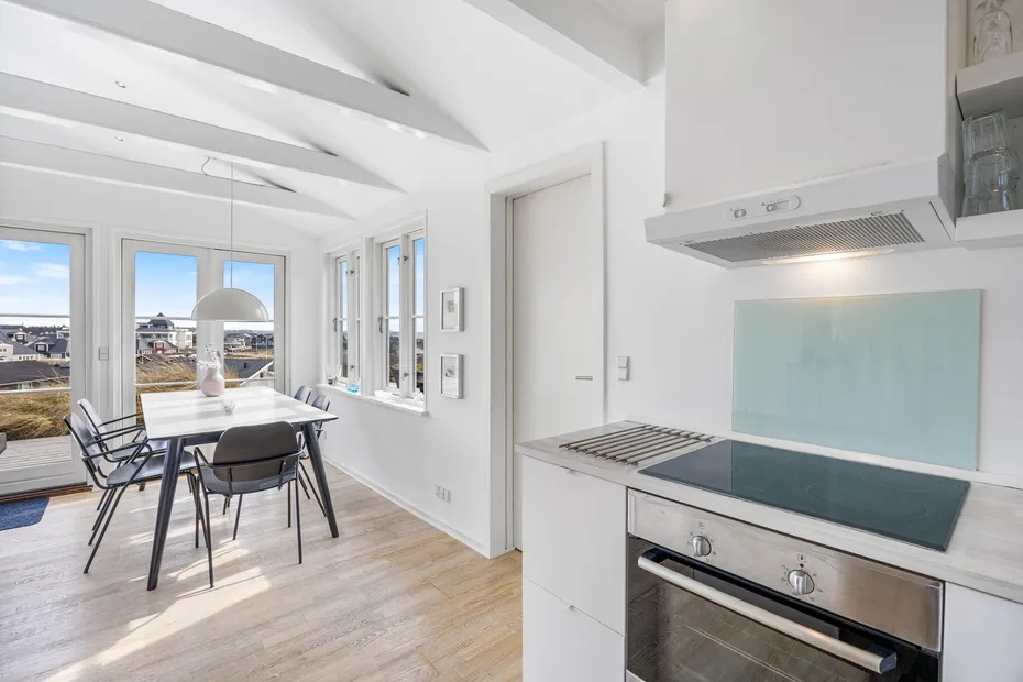 Una luminosa cocina abierta con comedor y una mesa junto a grandes ventanas.