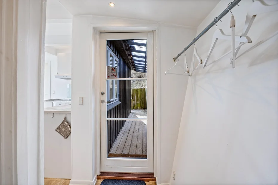Una entrada luminosa da a un pasillo exterior de madera, con un perchero junto a la pared.