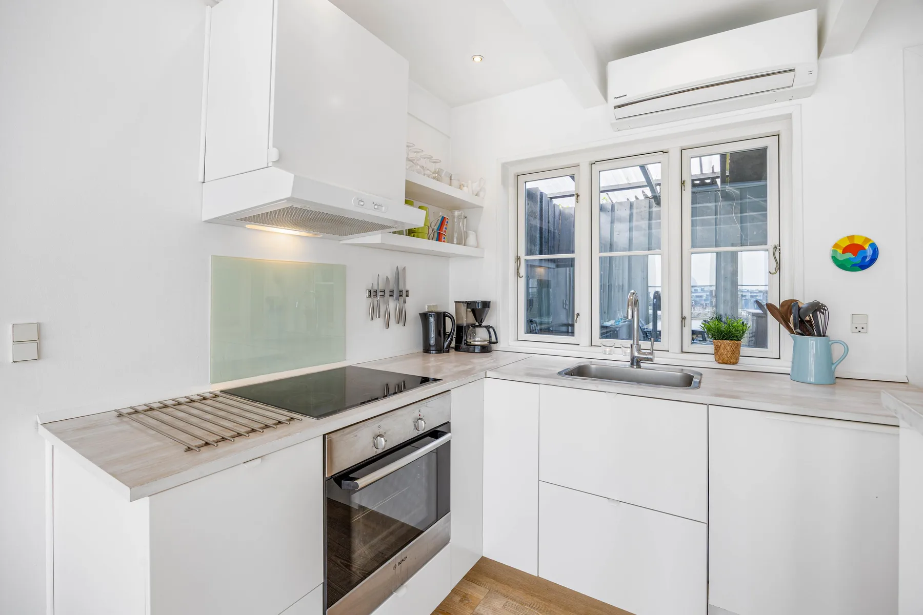 Una cocina luminosa con armarios blancos, una placa de cocina y una ventana.
