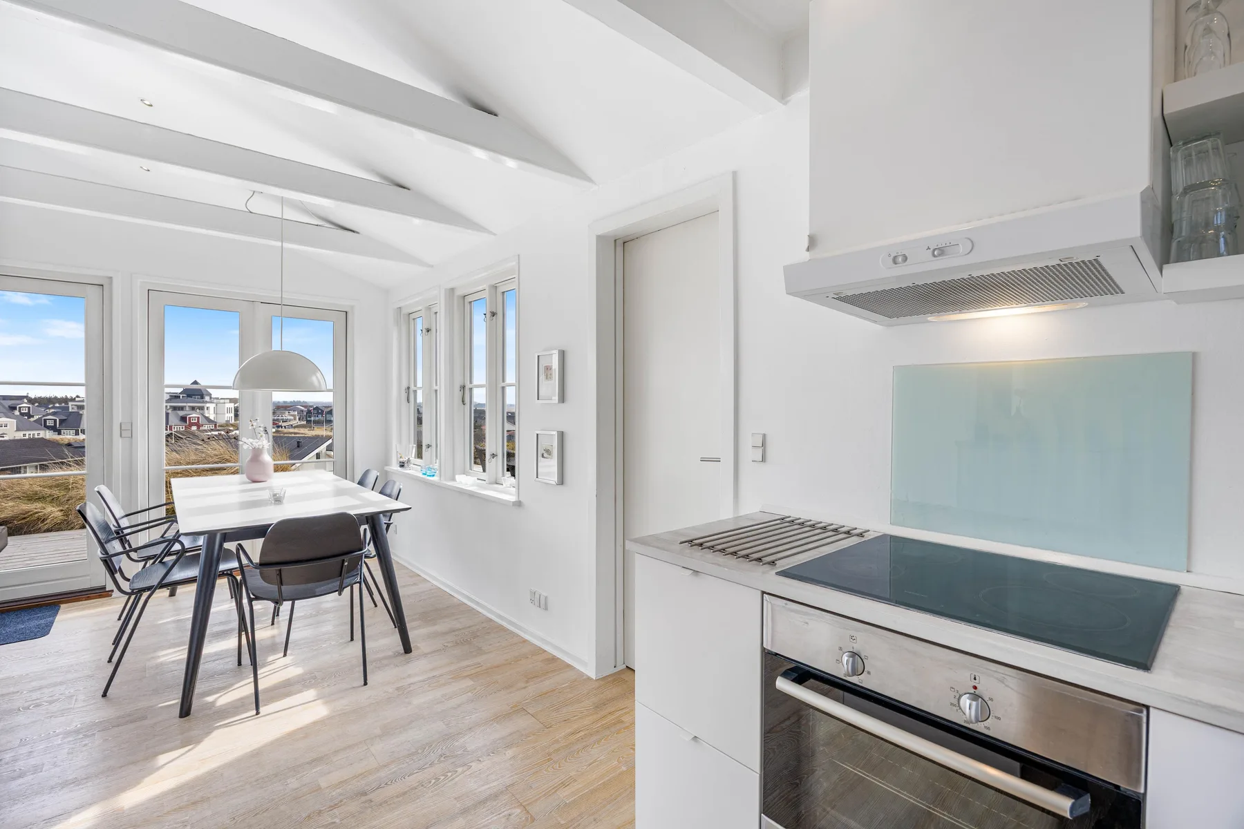 Una cocina y comedor luminosos, con una placa de cocina y una mesa junto a grandes ventanas.