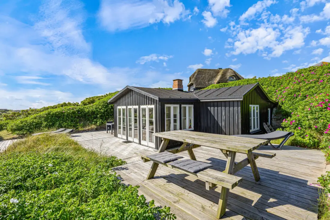 Una casa de exterior oscuro junto a una terraza de madera con una mesa de picnic.