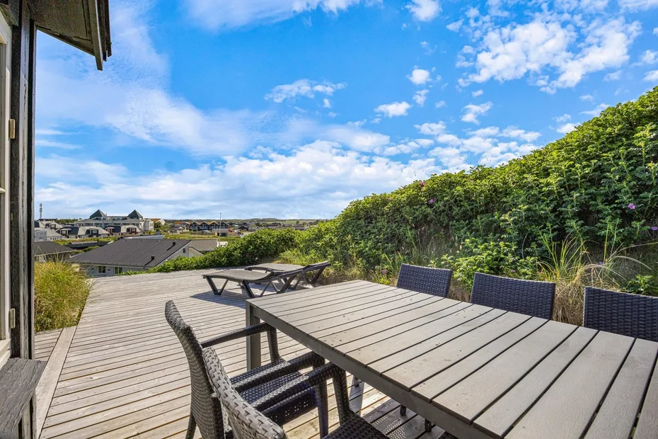 Comedor al aire libre en una terraza de madera con vistas a tejados cercanos.