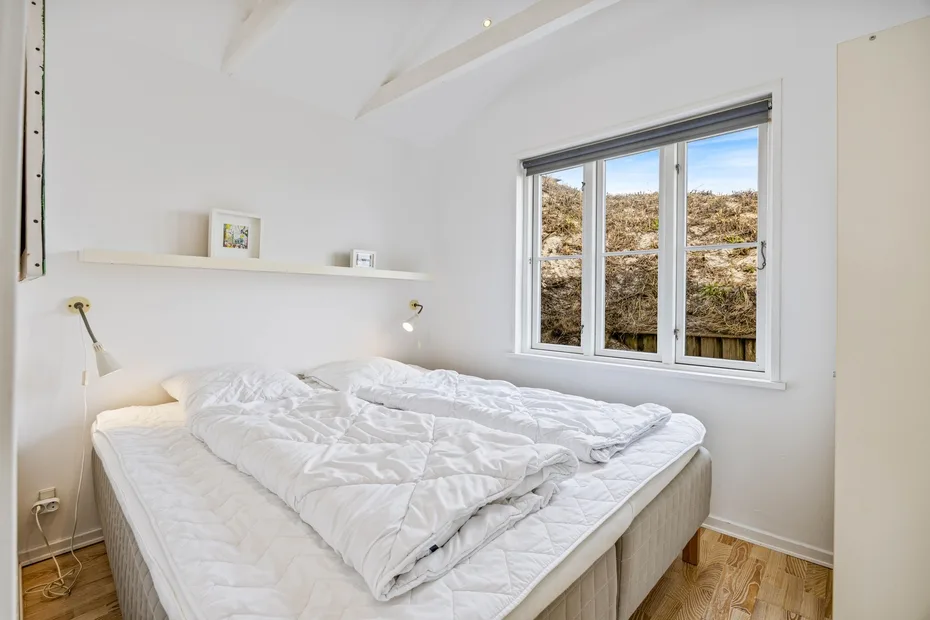 Un dormitorio luminoso con una cama grande bajo una ventana con vistas a una ladera.