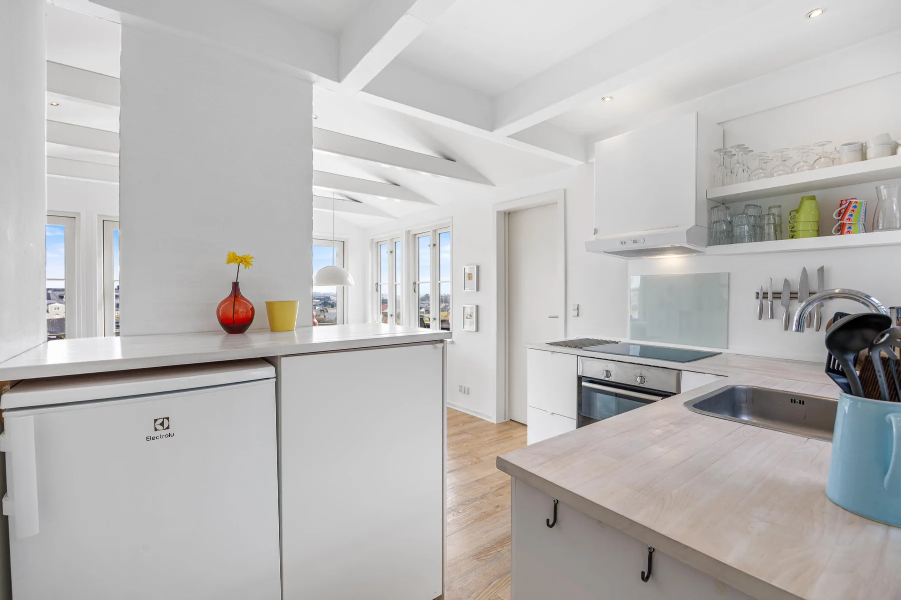 Una cocina blanca y luminosa con isla, encimera y estantes abiertos.