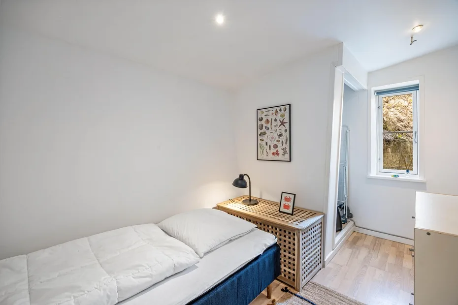 Un dormitorio luminoso con una cama, una mesita y una ventana.