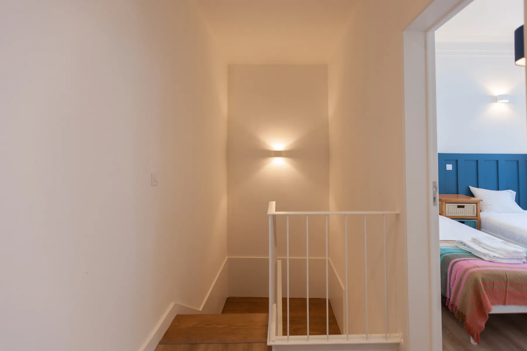 A stair landing with wooden steps, a railing, and a wall light.