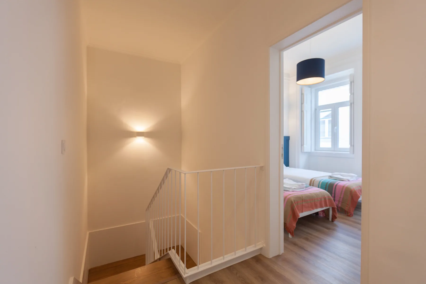 A bright stair landing opens onto a bedroom with colorful bedding.