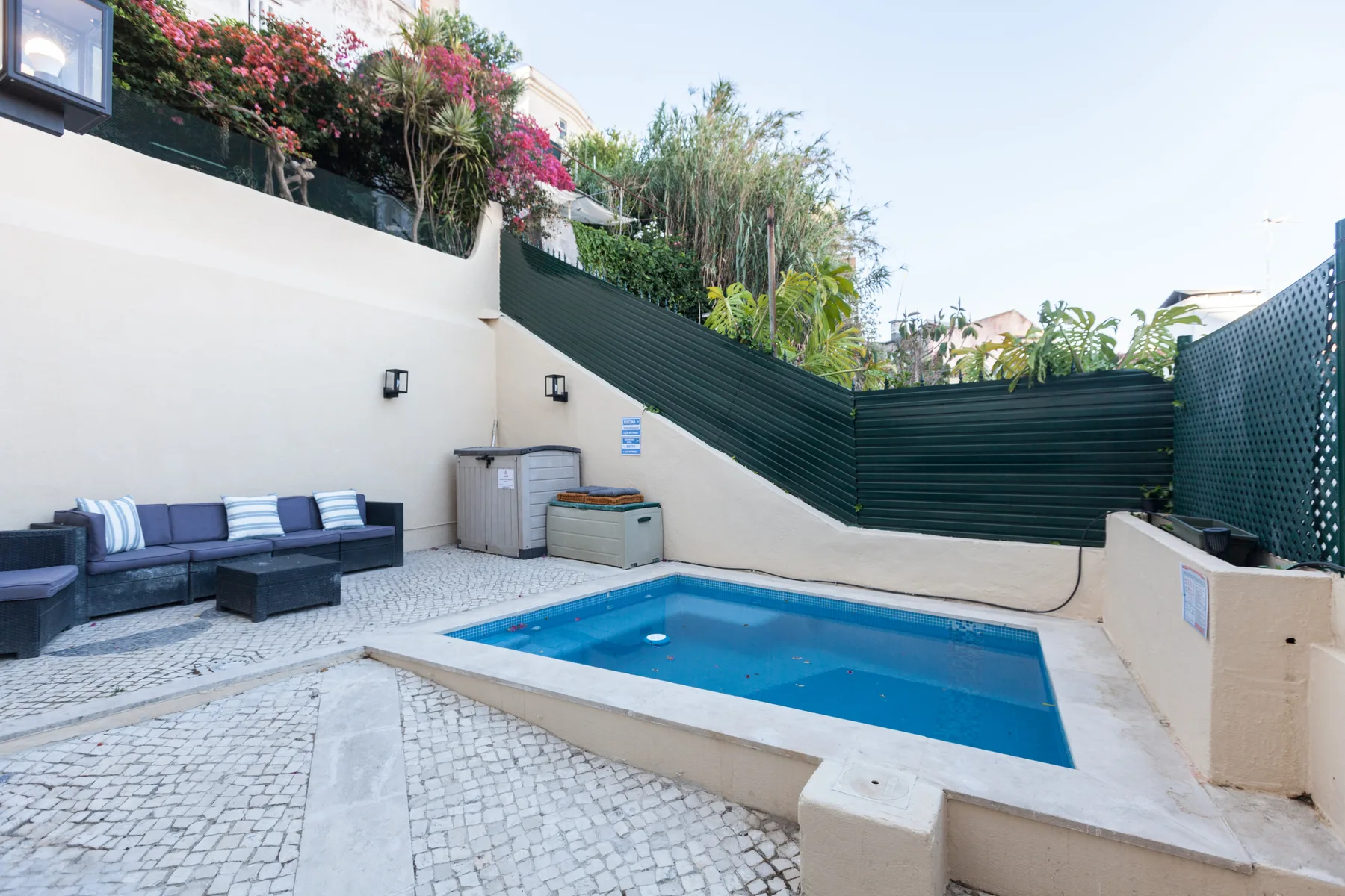 An outdoor pool sits beside cushioned seating in a paved courtyard.