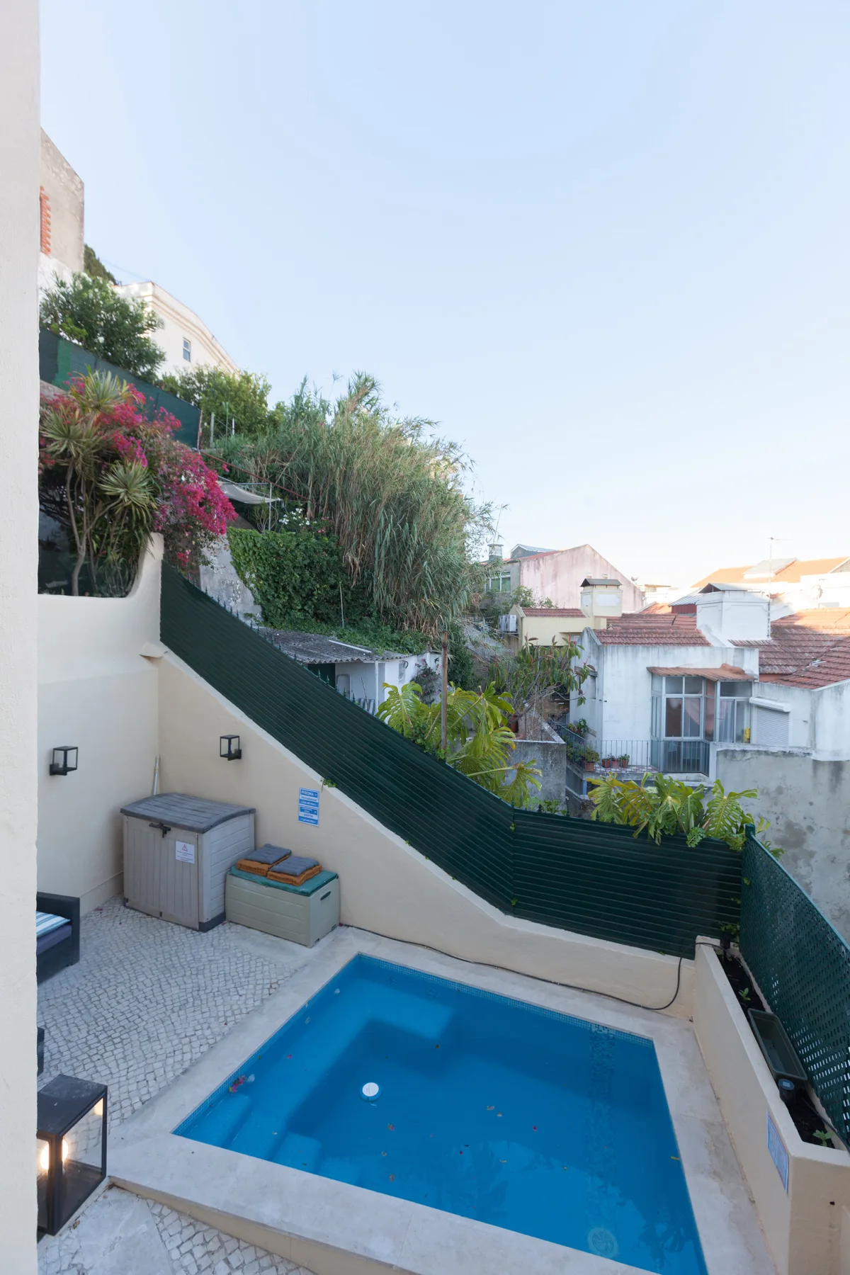 A small outdoor swimming pool sits on a paved terrace beside a planted boundary.