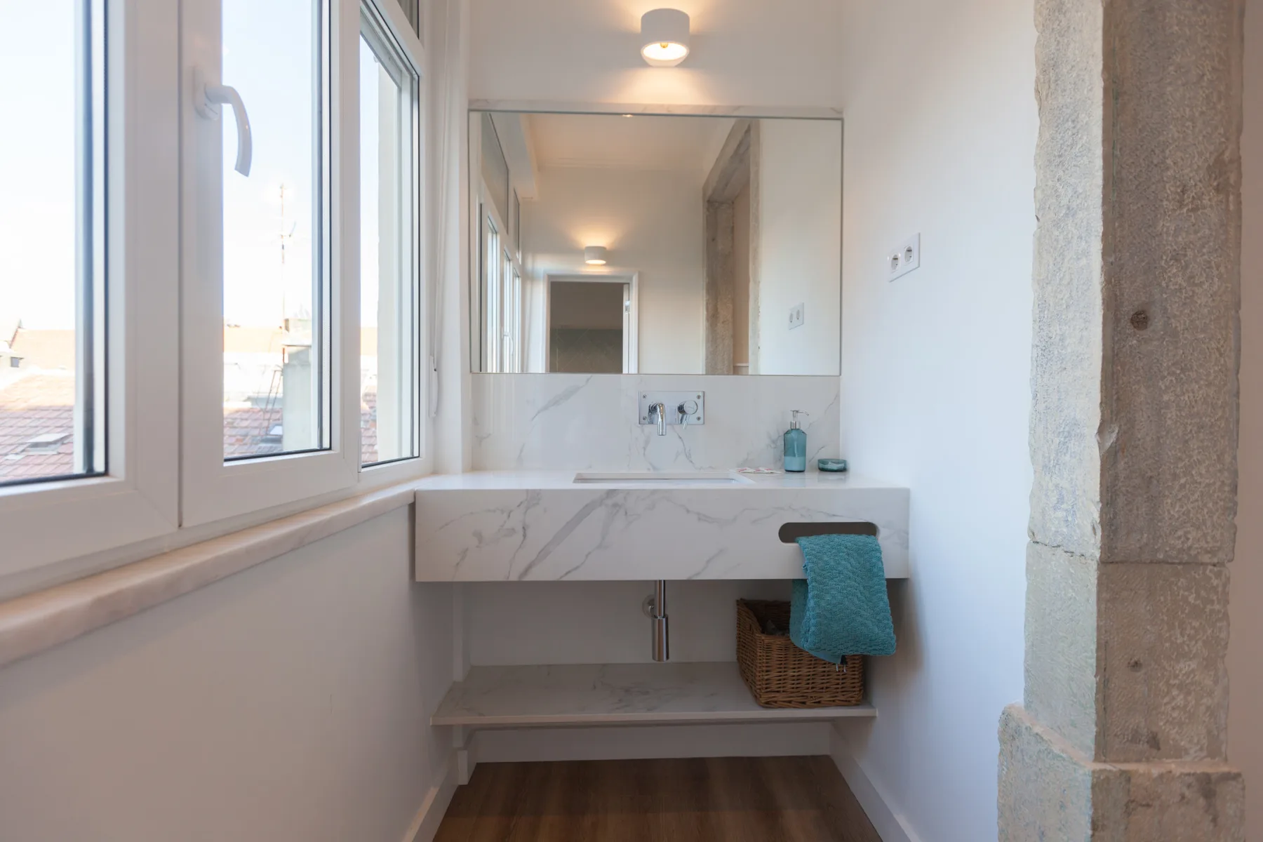 A bright bathroom vanity sits beneath a large mirror beside tall windows.