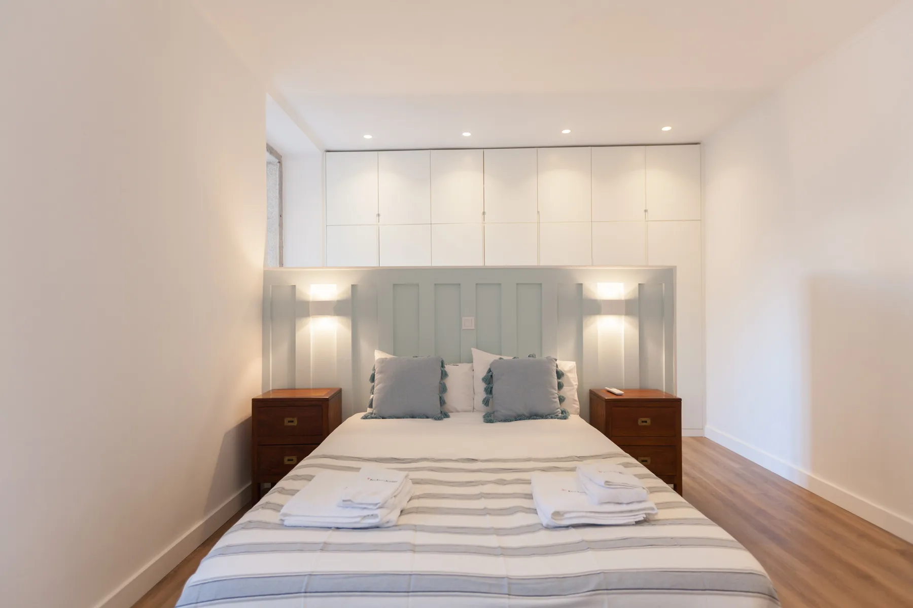 A bright bedroom with a neatly made bed and built-in cabinets.