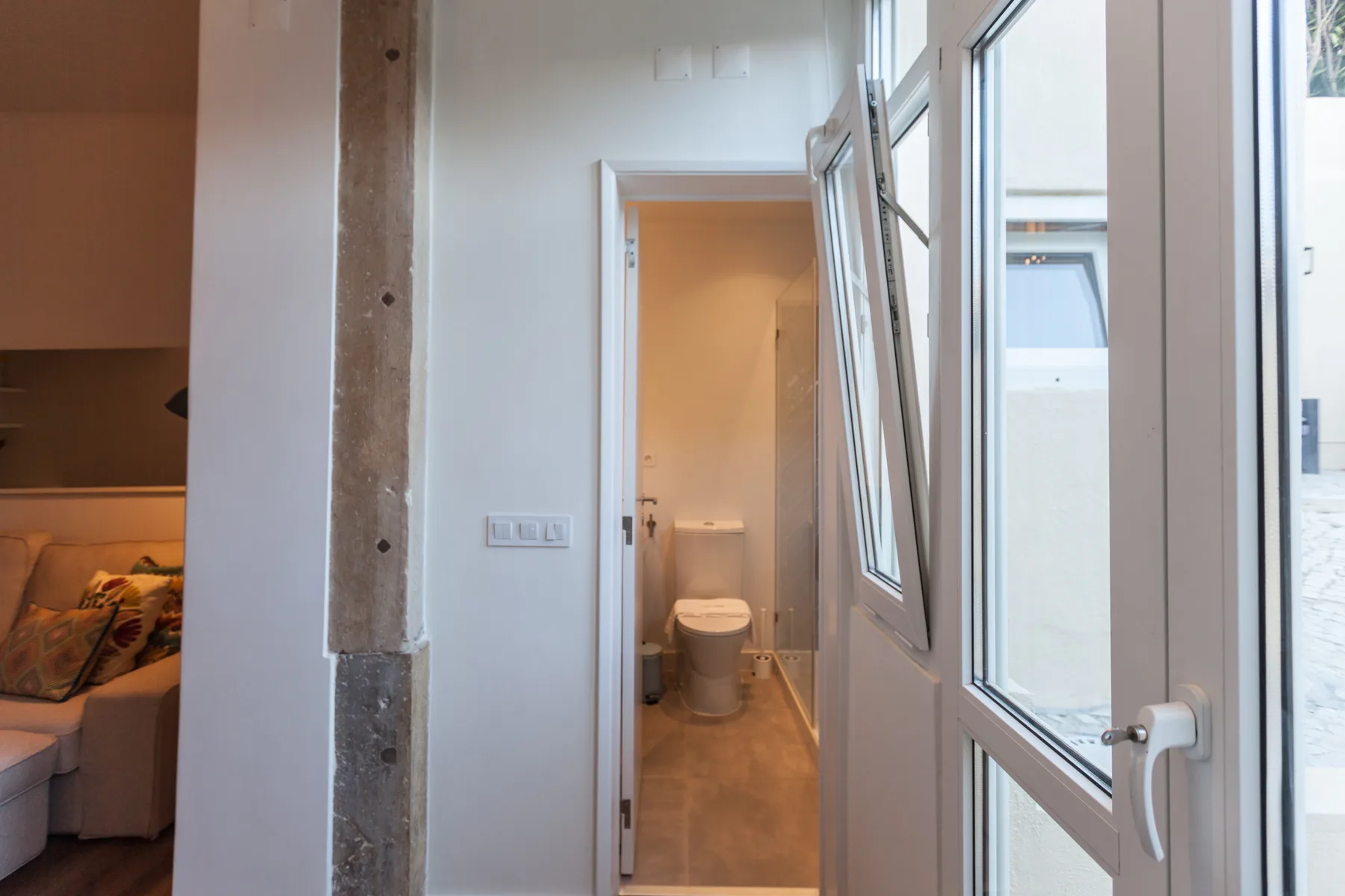 A bathroom is visible through an open doorway beside a bright window.
