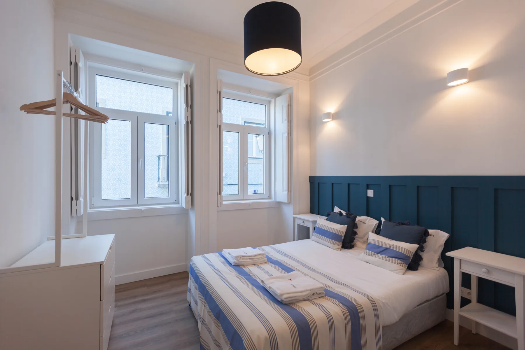 A bedroom with a bed, blue headboard, and windows.