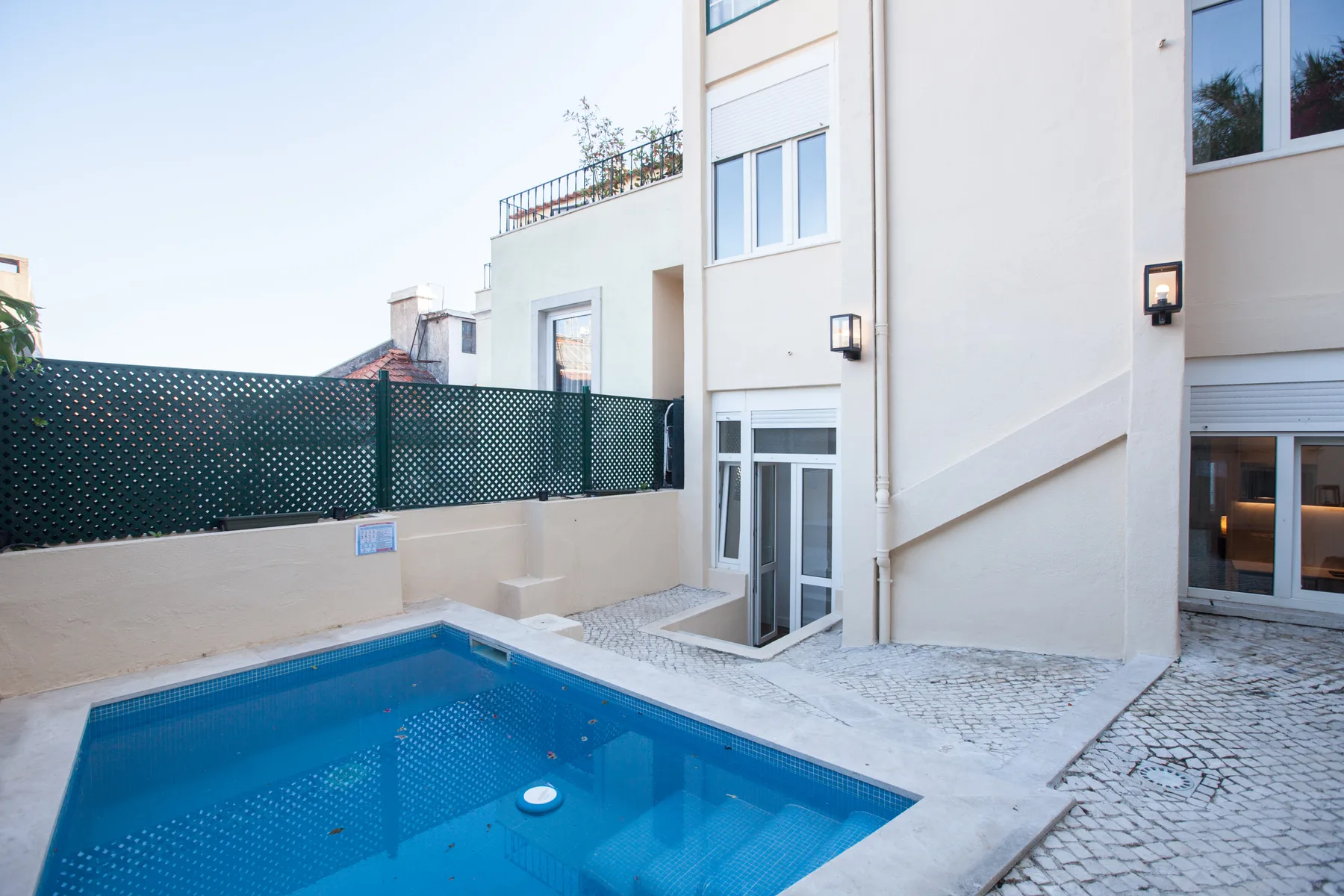 A small outdoor pool sits beside a modern white building and paved terrace.