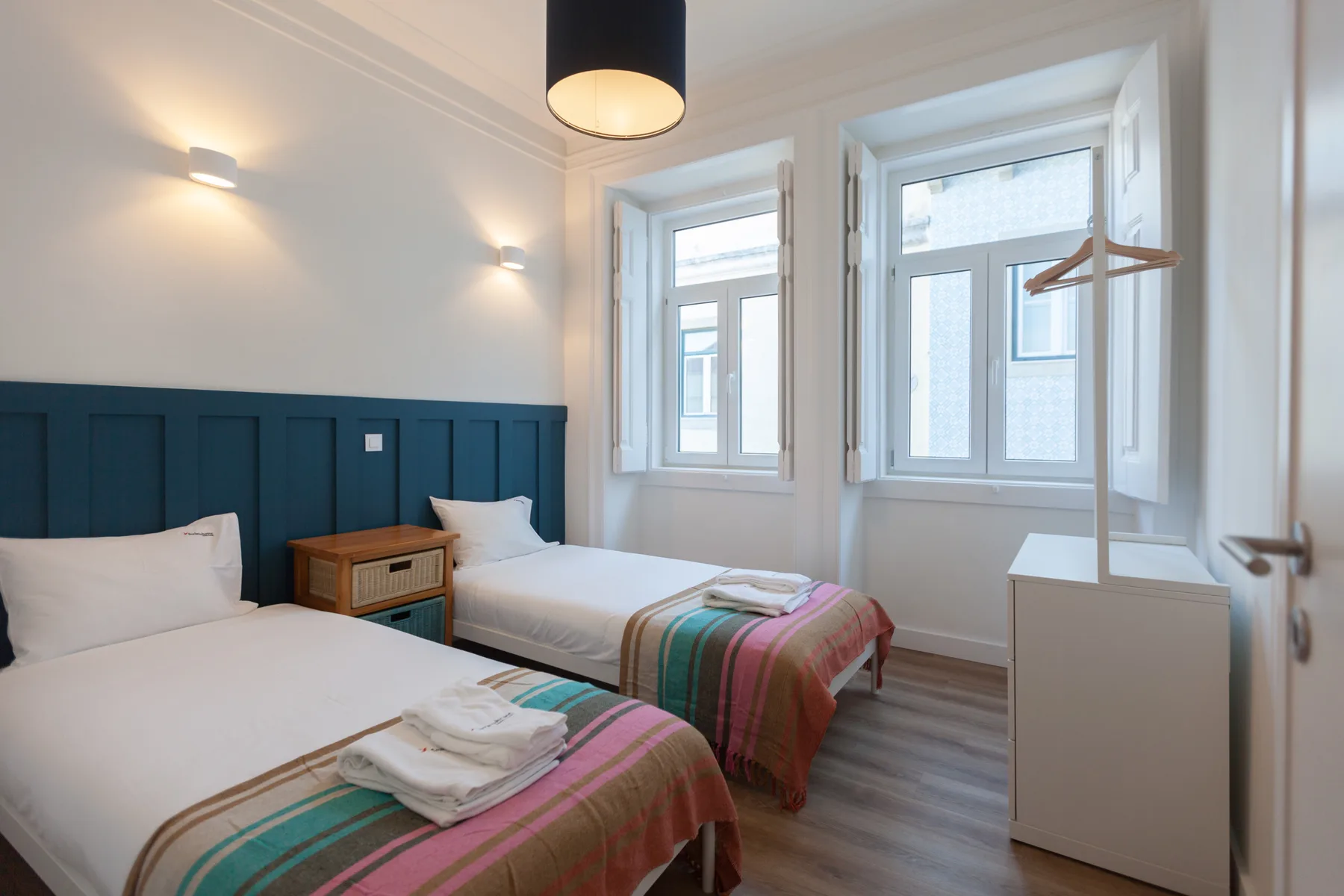 A bright bedroom with two beds, a window, and a small dresser.
