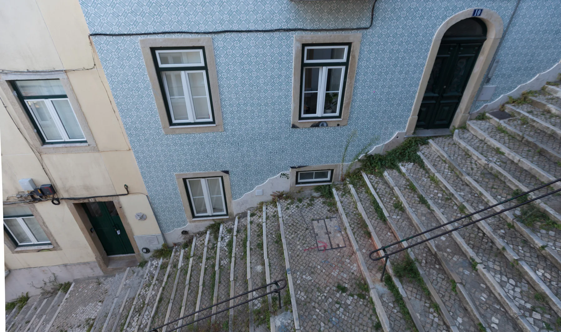A cobblestone stairway passes between buildings with blue tiled walls and dark doorways.
