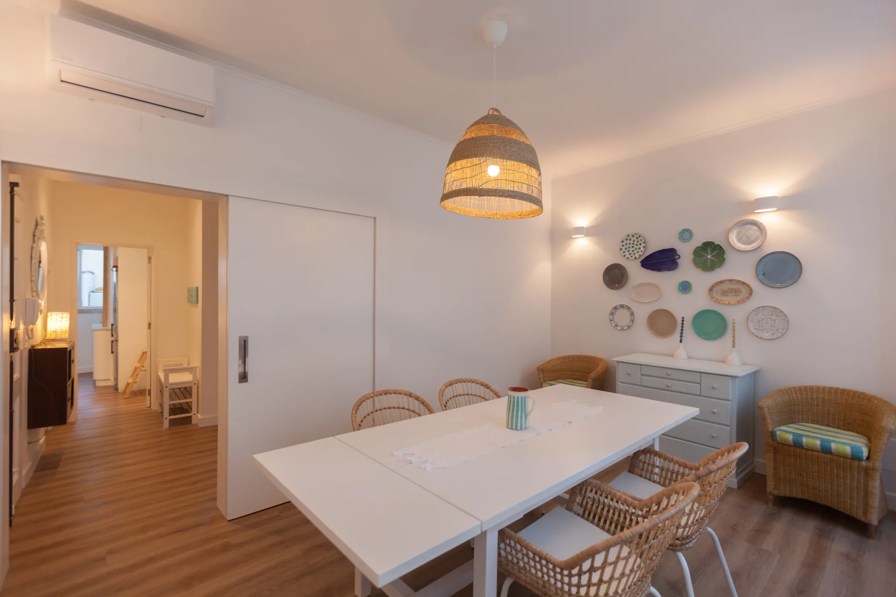 A dining area with a white table, woven seating, and decorative plates on the wall.