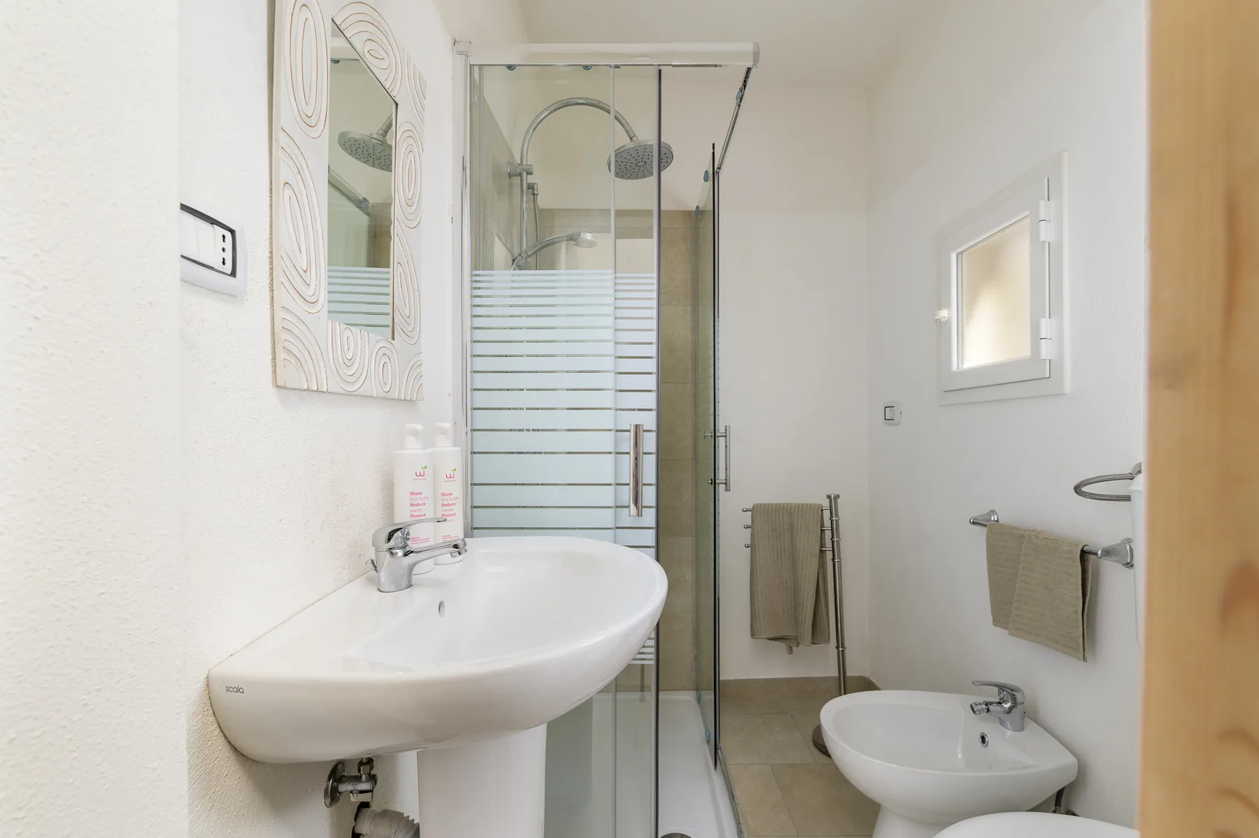 A bright bathroom with a sink, glass shower, and bidet.