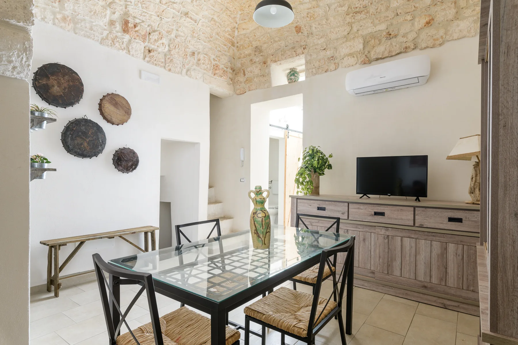 A dining area with a glass table and a television on a wooden cabinet.