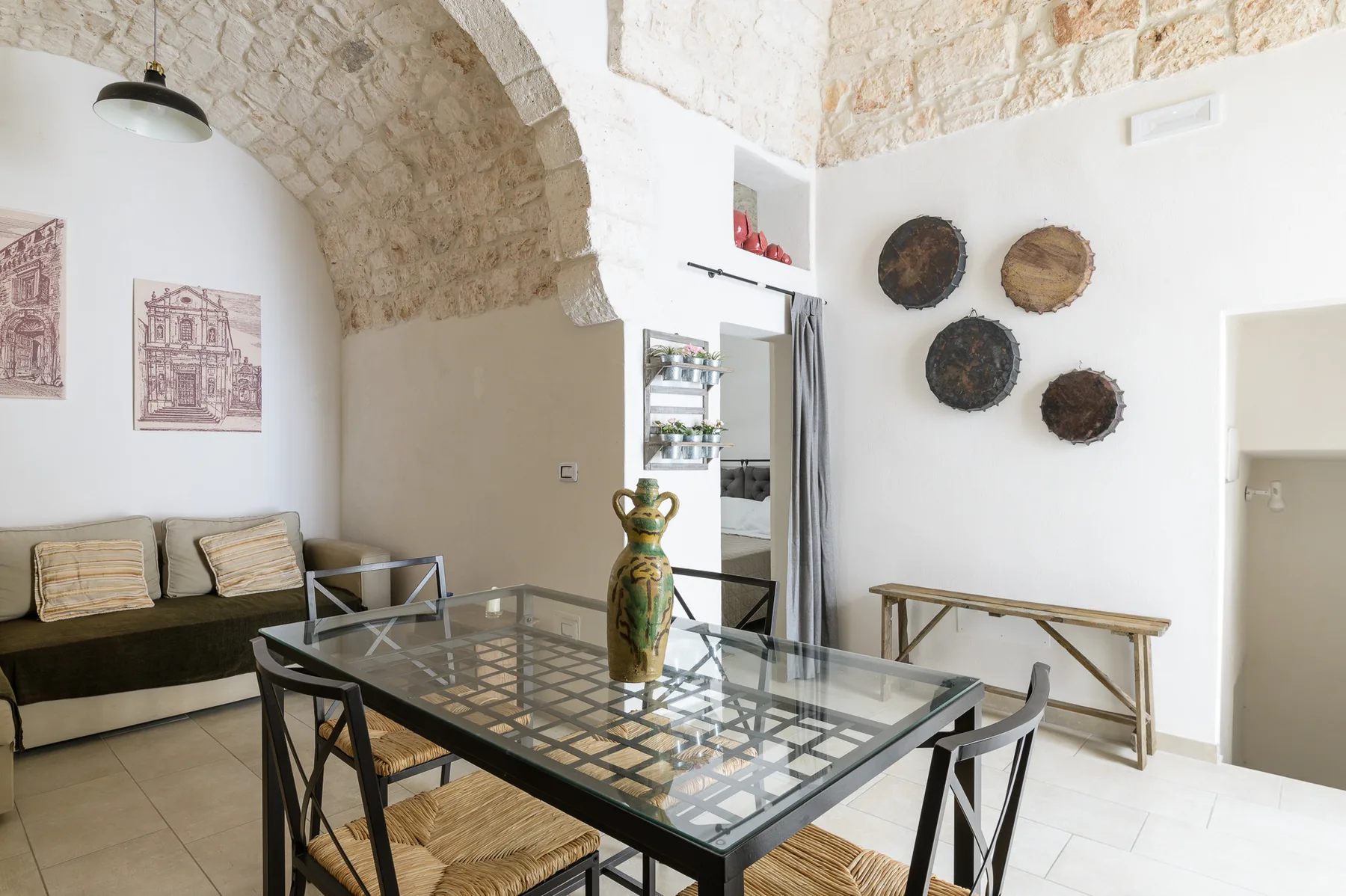 A dining area beneath a stone arch, with a glass table and wall decorations.