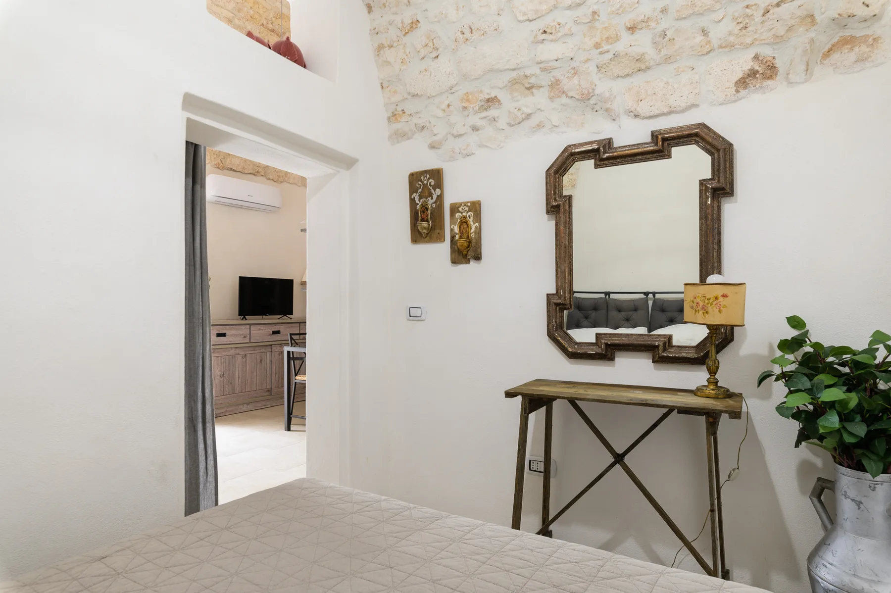 A bright bedroom with a bed, a mirrored console table, and an open doorway.