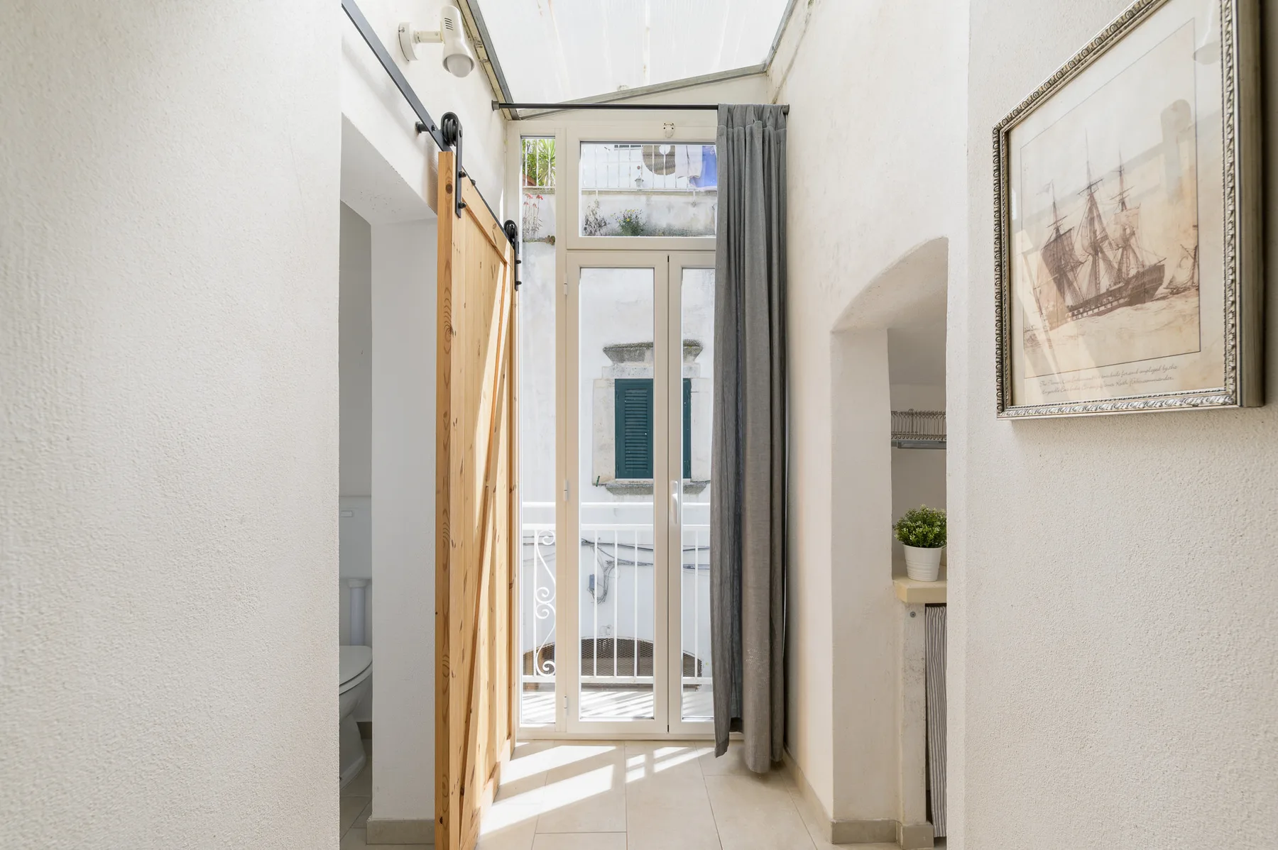 A bright entryway with glass doors, a curtain, and framed wall art.