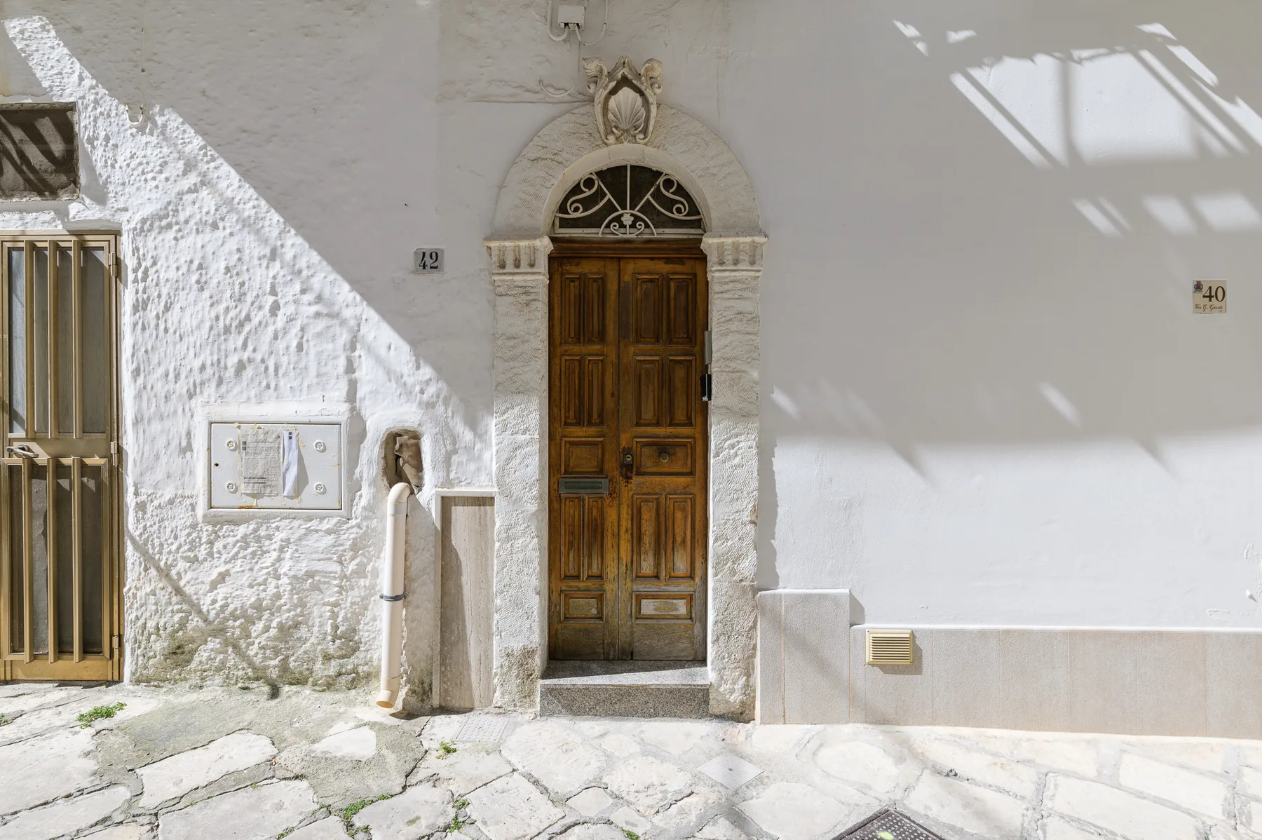 A sunlit white facade features a dark wooden door beneath a decorative stone arch.