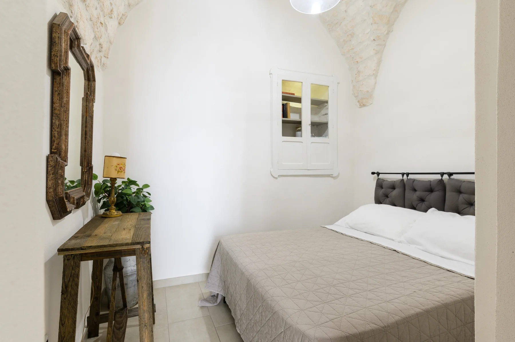 A bedroom with a bed beneath an arched ceiling and a small window.