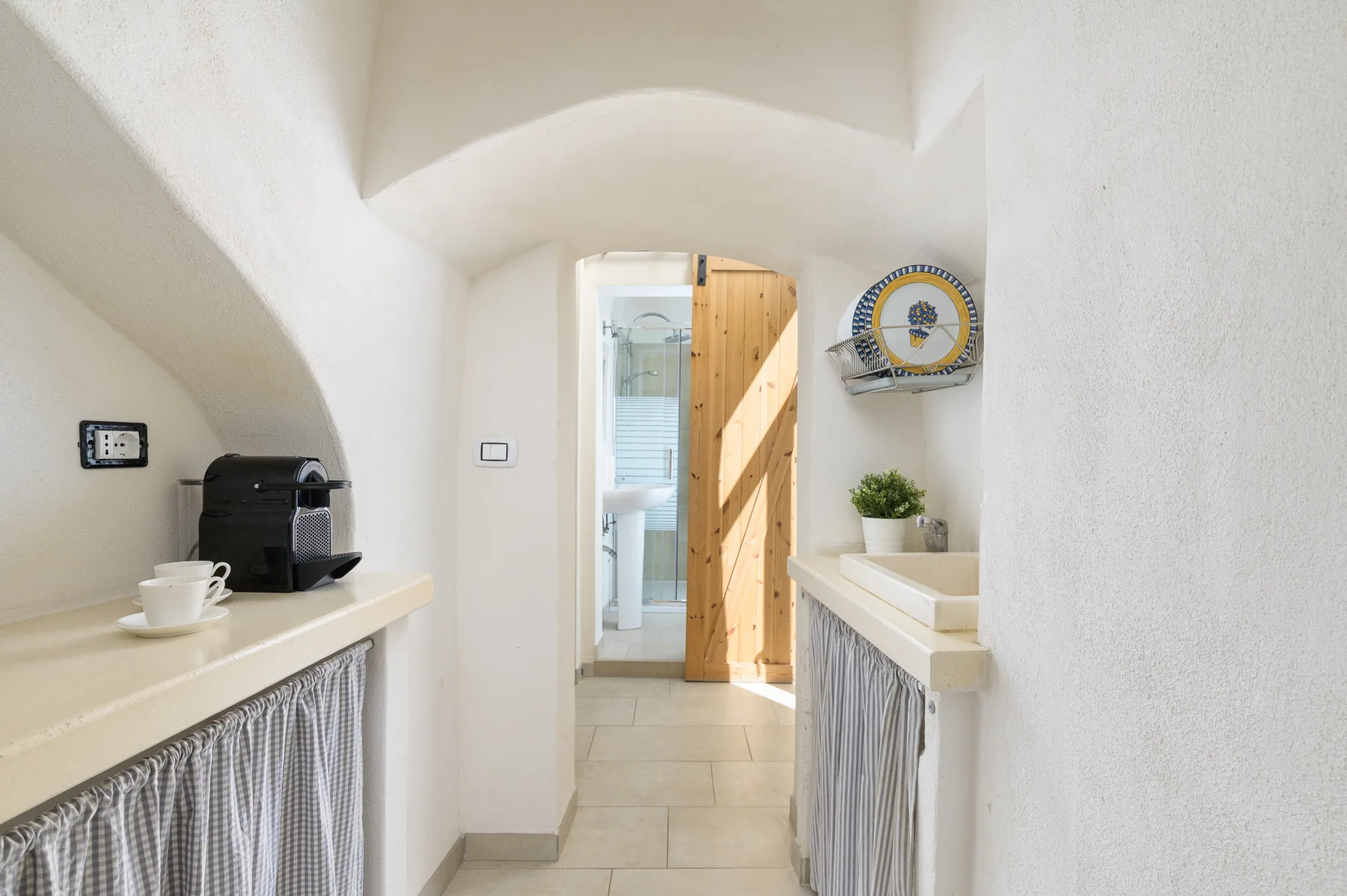 A bright interior passage with a coffee machine on a counter and a wooden door.