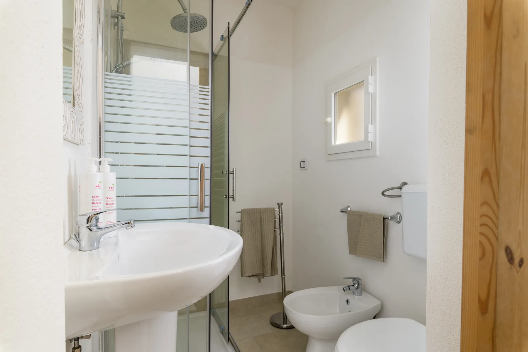 A bathroom with a glass shower, sink, toilet, and bidet.