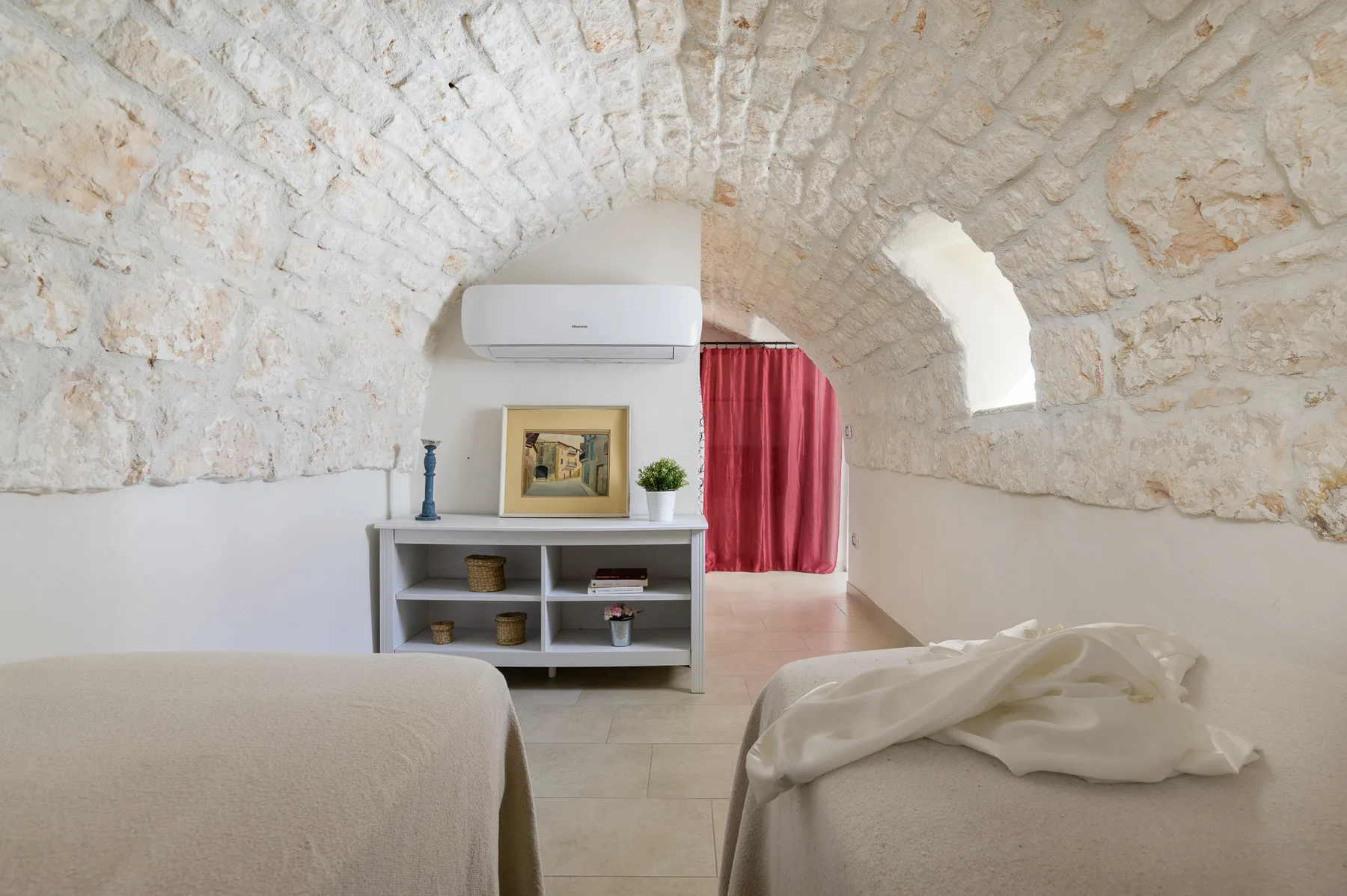 A bedroom with a stone vaulted ceiling, shelving, and a red curtain.