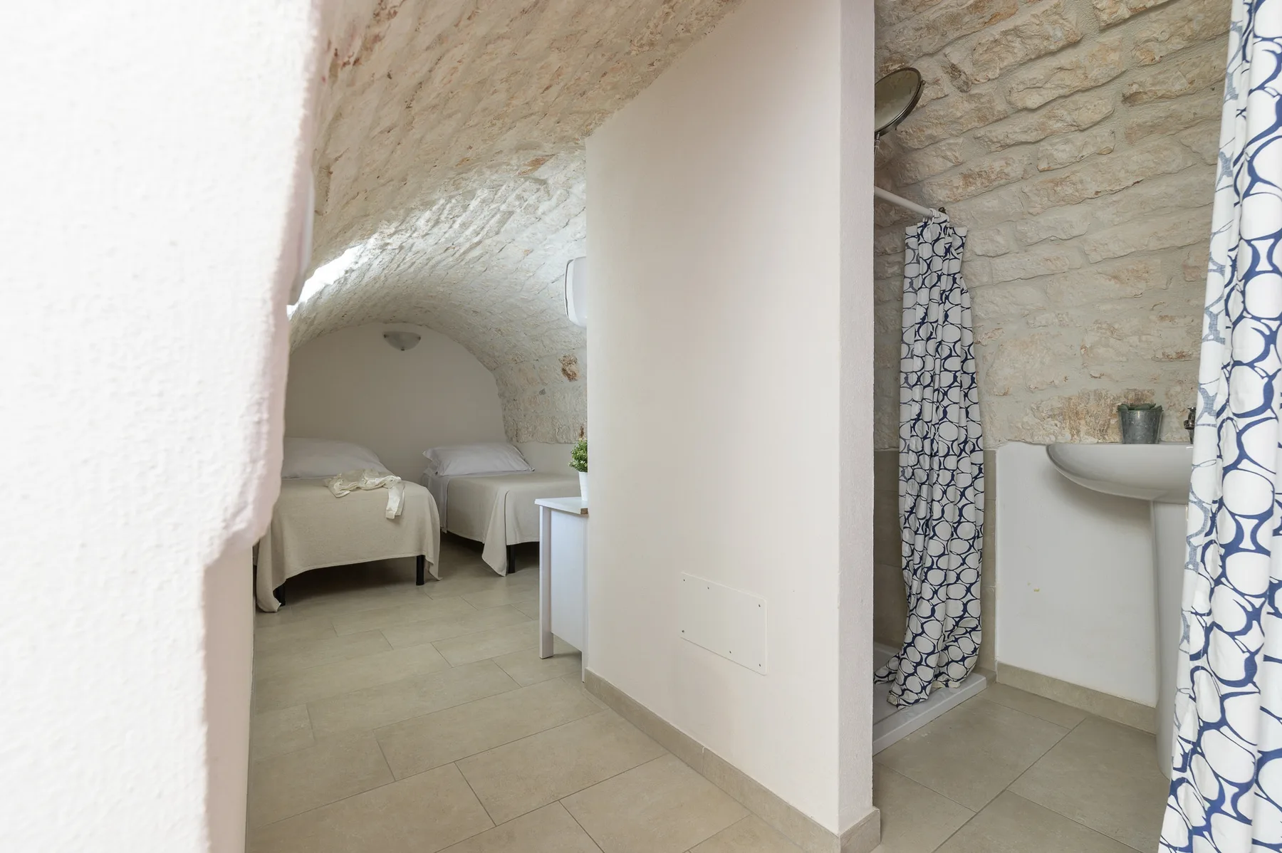 A bedroom with two beds and an adjoining bathroom beneath a stone ceiling.