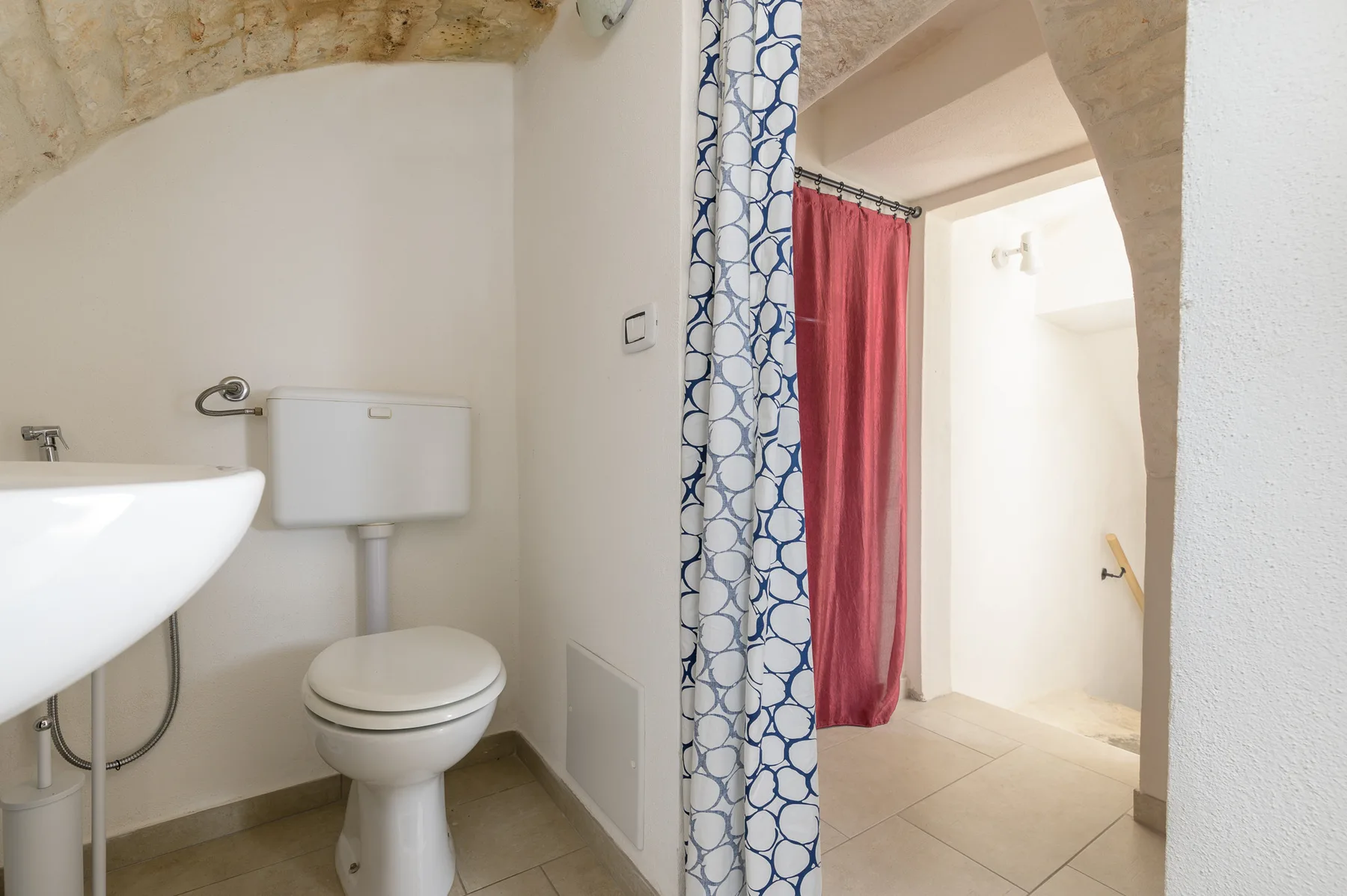 A bathroom with a sink and toilet beside a curtained doorway.