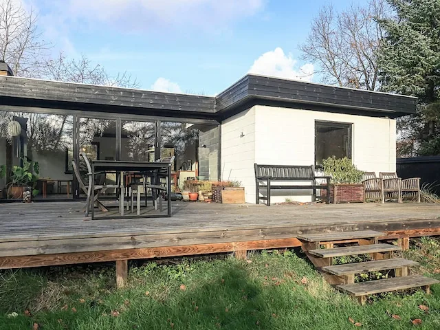 A modern house opens onto a wooden deck with outdoor seating.