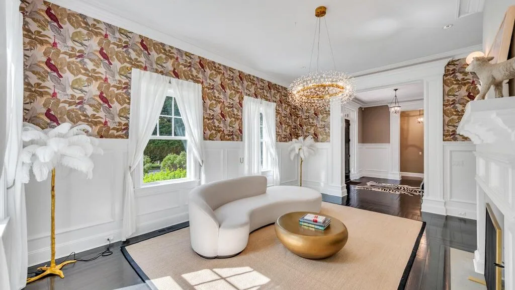 Una sala luminosa con papel tapiz estampado, asientos blancos y una mesa de centro redonda.
