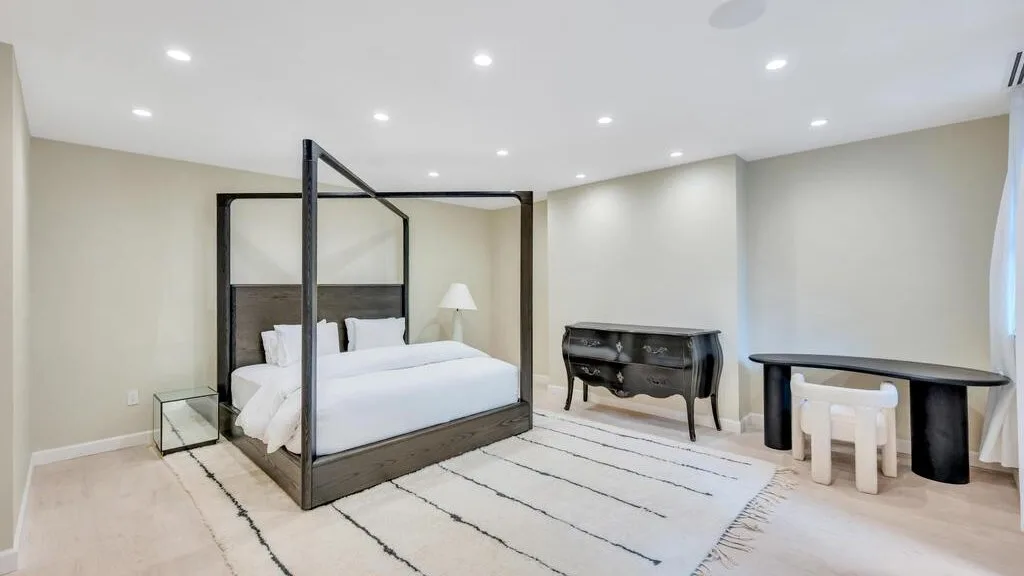 Un dormitorio con una cama con dosel, una alfombra y muebles oscuros.