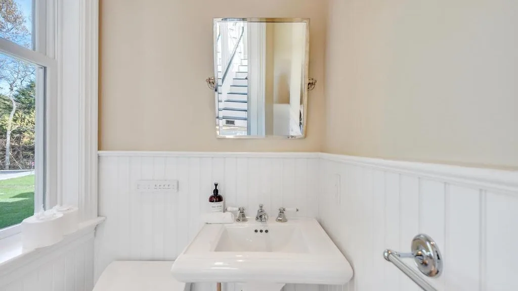 Un lavabo de baño con espejo rectangular está junto a una ventana.