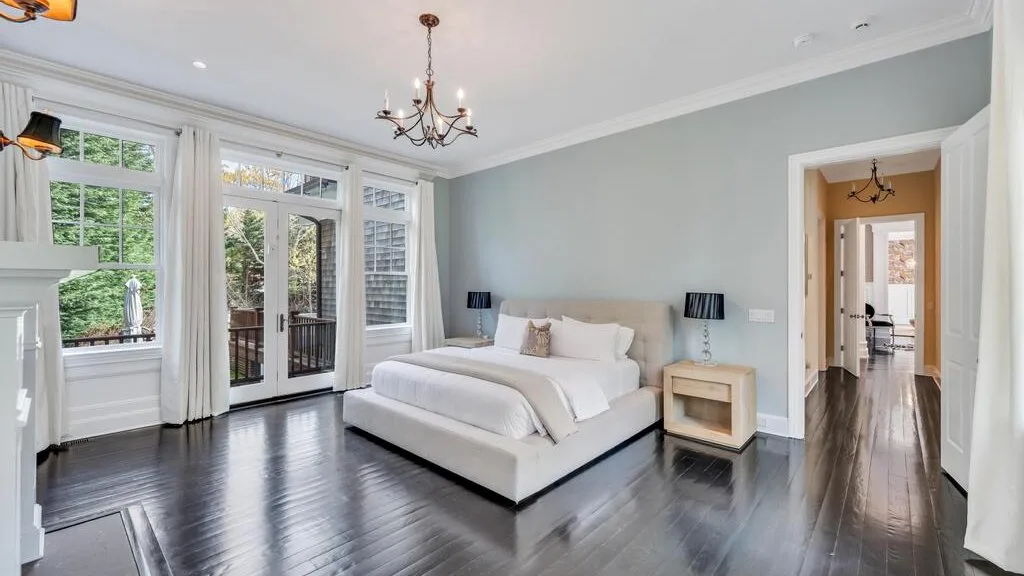 Un dormitorio luminoso con una cama junto a ventanas altas y puertas de vidrio.