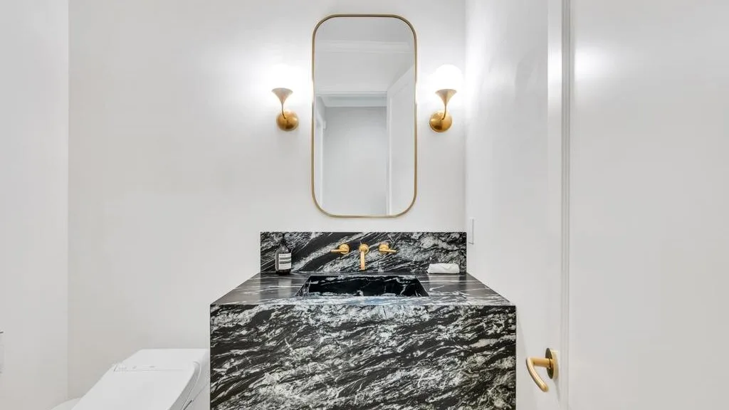 Un lavabo de baño con una encimera oscura estampada y un espejo.