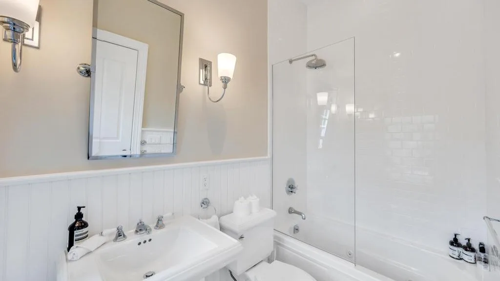 Un baño luminoso con lavabo, espejo y bañera con ducha.