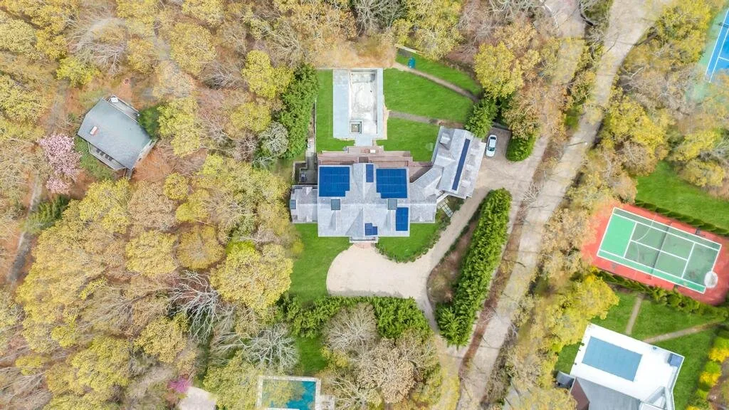 Una vista aérea muestra una casa, árboles alrededor y una cancha de tenis cercana.