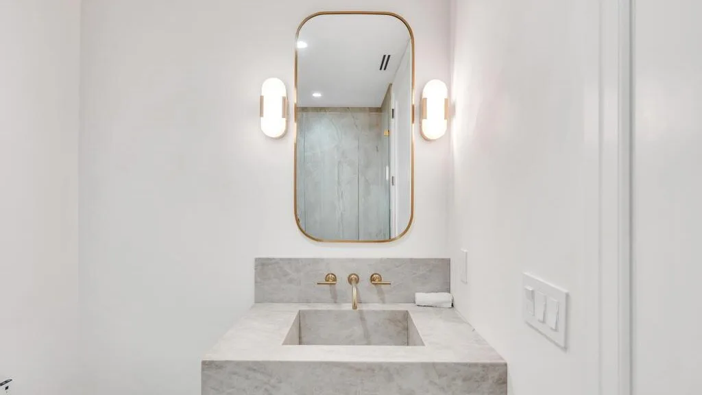 Un tocador de baño con lavabo rectangular, espejo y luces de pared.