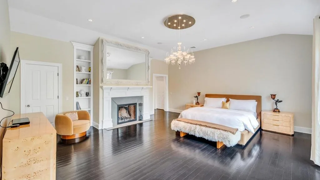 Un dormitorio luminoso cuenta con una cama grande, una chimenea y suelo oscuro.