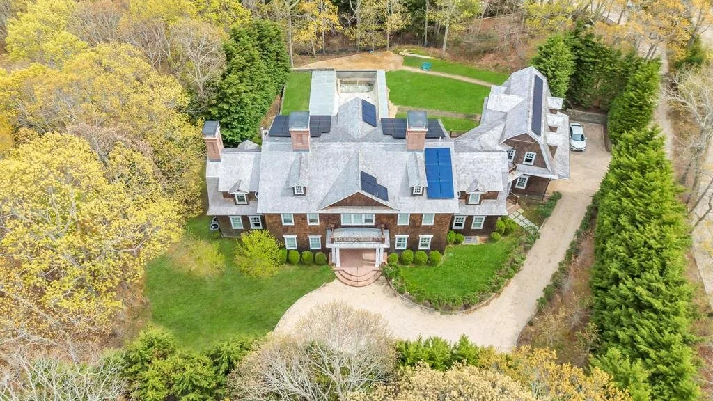 Una vista aérea muestra una casa grande rodeada de césped, árboles y un camino curvo.
