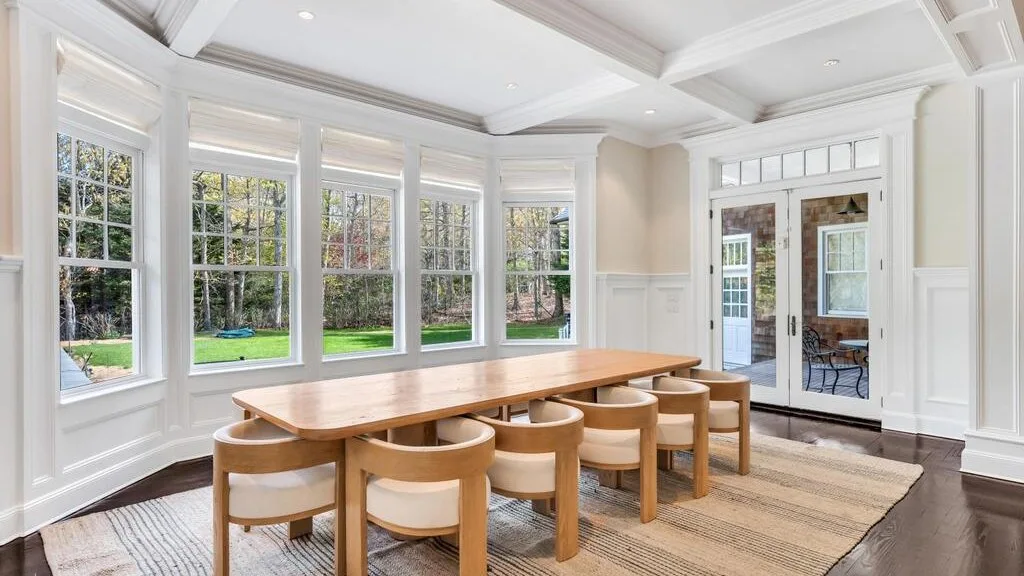 Un comedor luminoso con una mesa larga de madera y grandes ventanas.