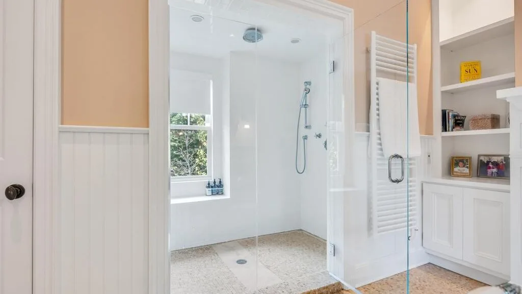 Un baño luminoso con ducha de vidrio, ventana y almacenamiento integrado.